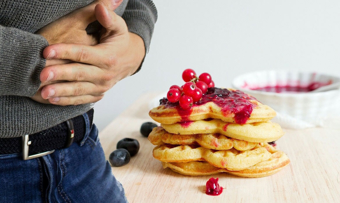Man holding stomach with waffles on table