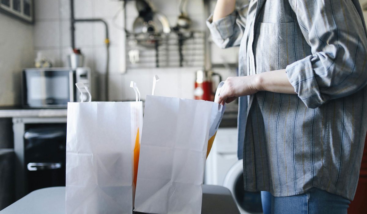 A person looking into two grocery bags on a kitchen table