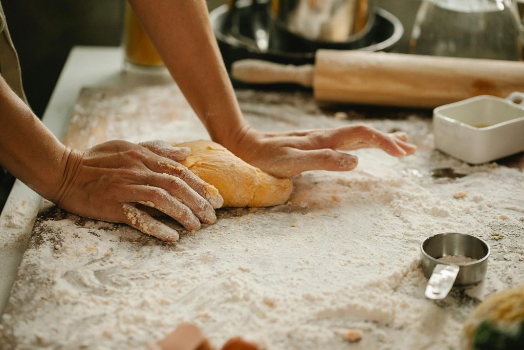 Close-up of hands kneading dough on a floured surface, showing a person preparing food in the kitchen.