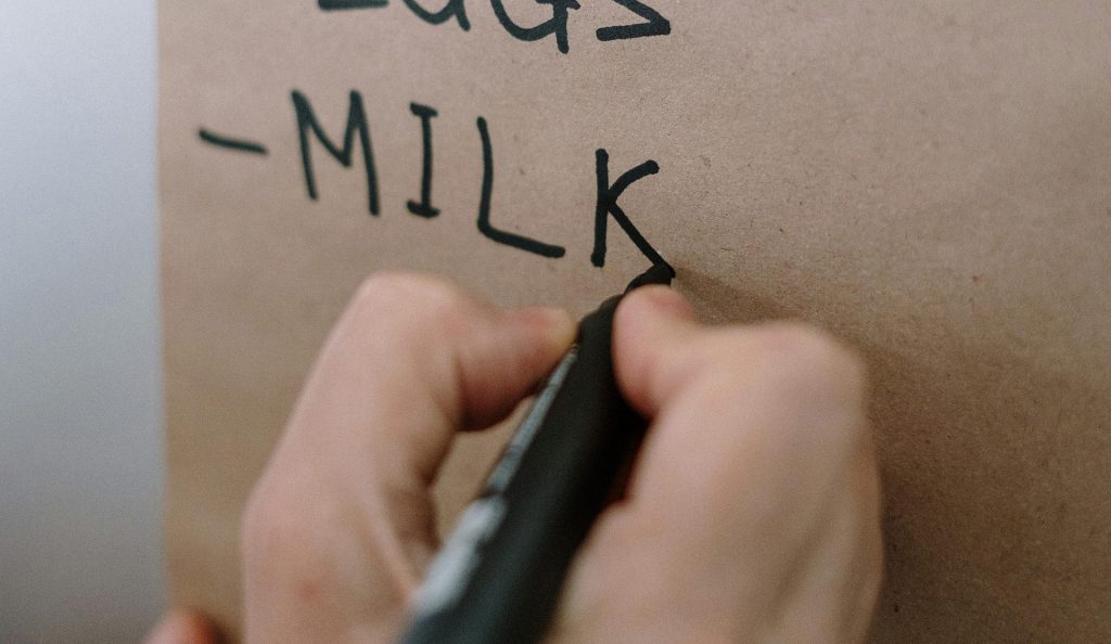 Close up of grocery list with someone writing Milk