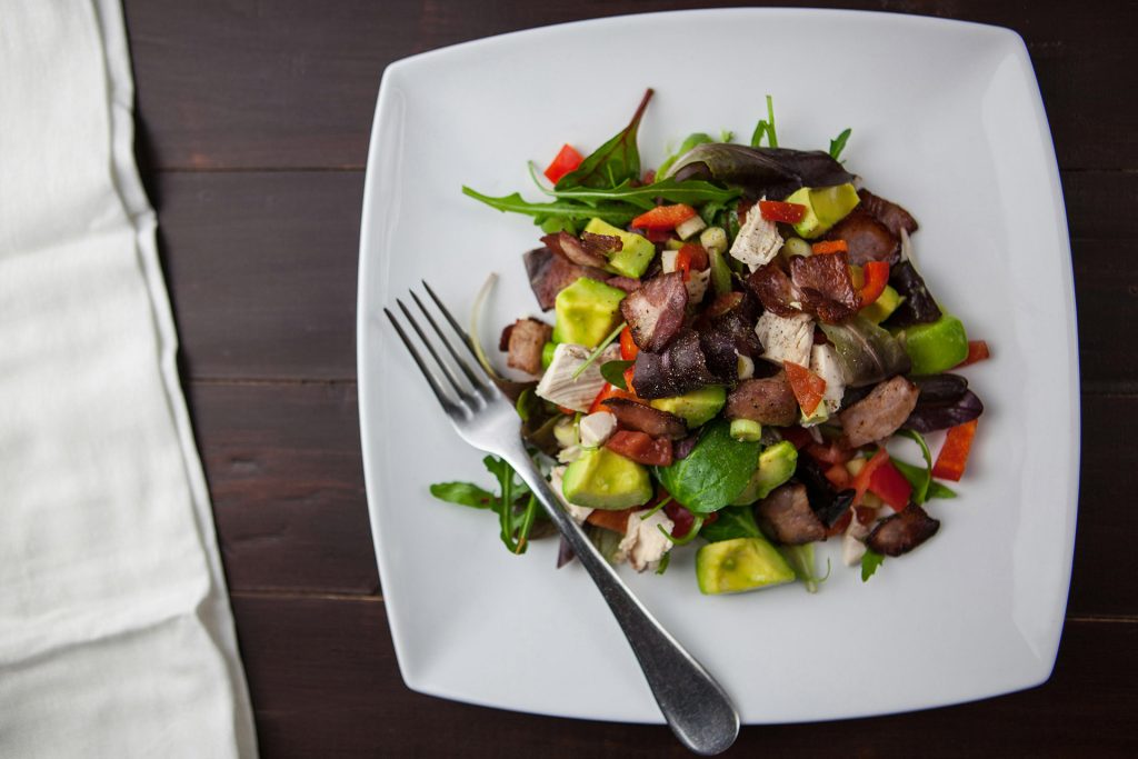 A plate of mixed salad with avocado, vegetables, and protein pieces, representing a balanced meal often used in eating disorder recovery and meal support.