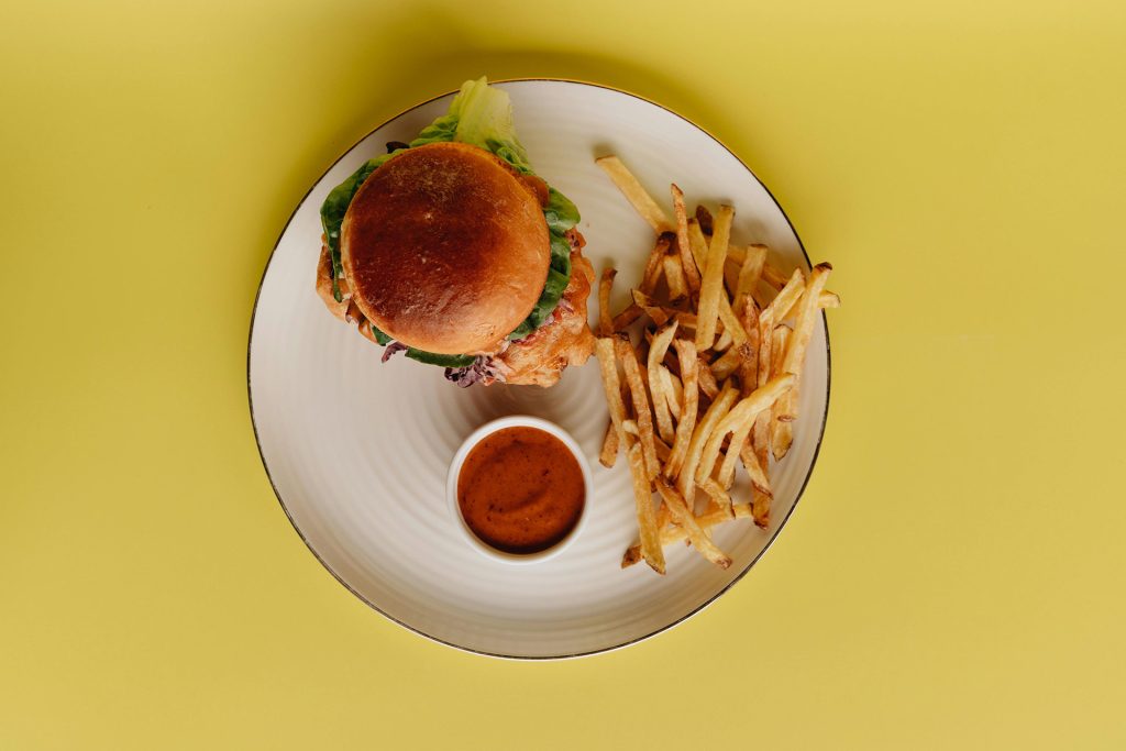 Burger and fries on plate on yellow table