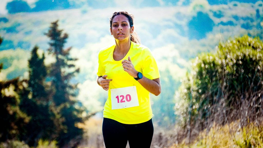 Athlete running outdoors in a race, wearing a bright yellow shirt and a race bib.