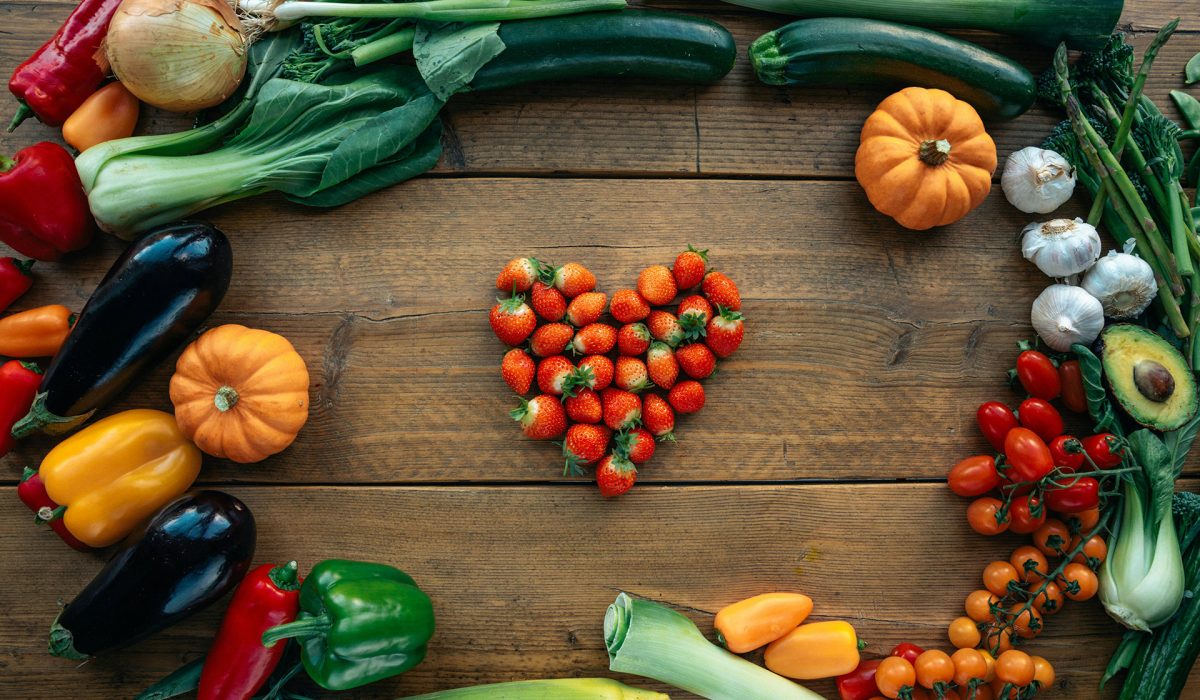 Table with vegetables surrounding a strawberries in the shape of a heart