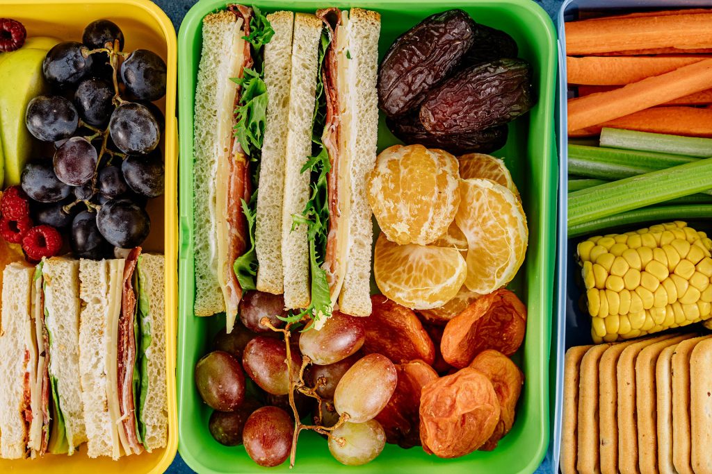 Three lunchboxes packed with sandwiches and fruit