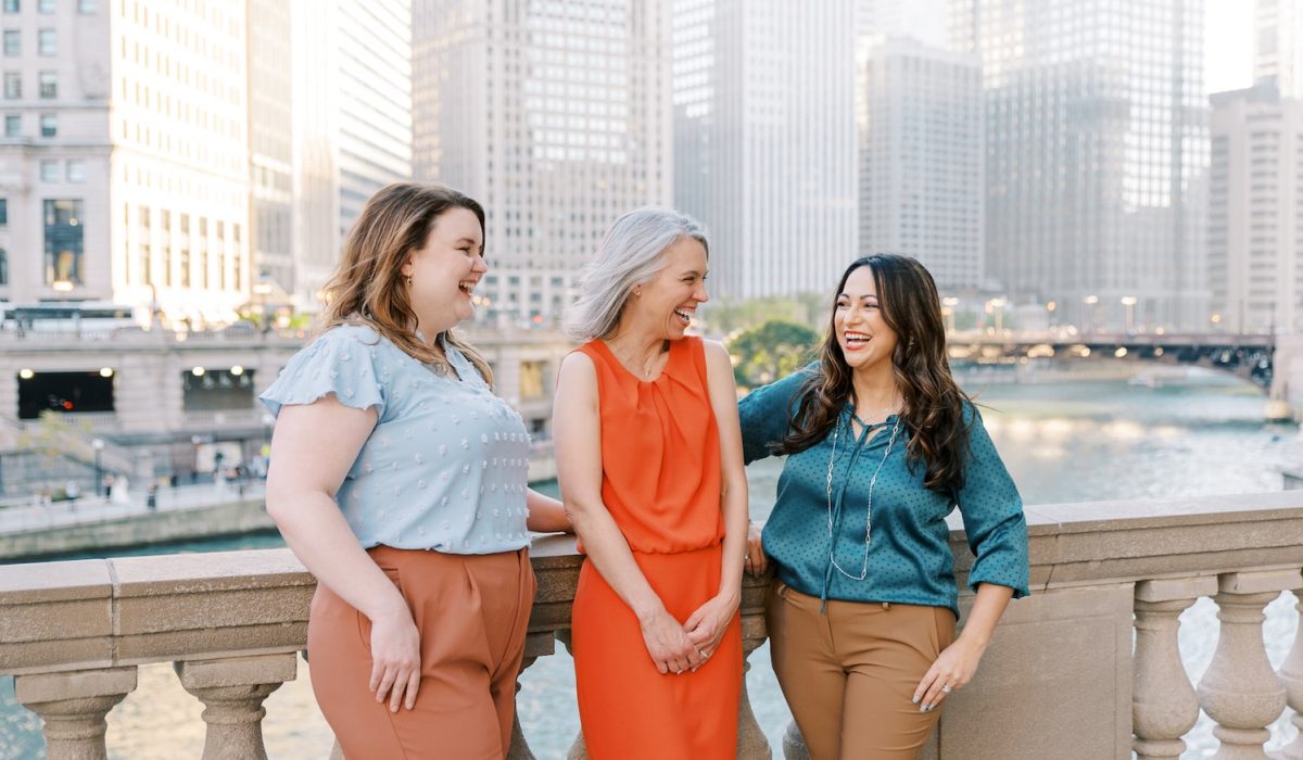 Three women smiling at each other standing along the Chicago River