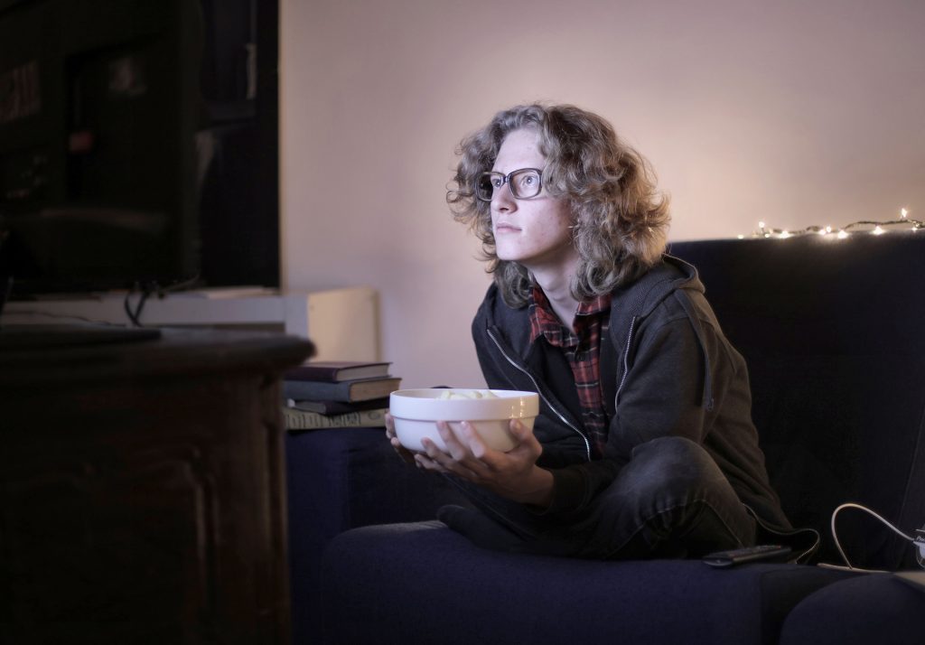 Woman with a bowl of food sitting on couch watching TV