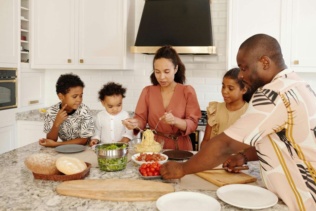 Family in kitchen with mother serving pasta