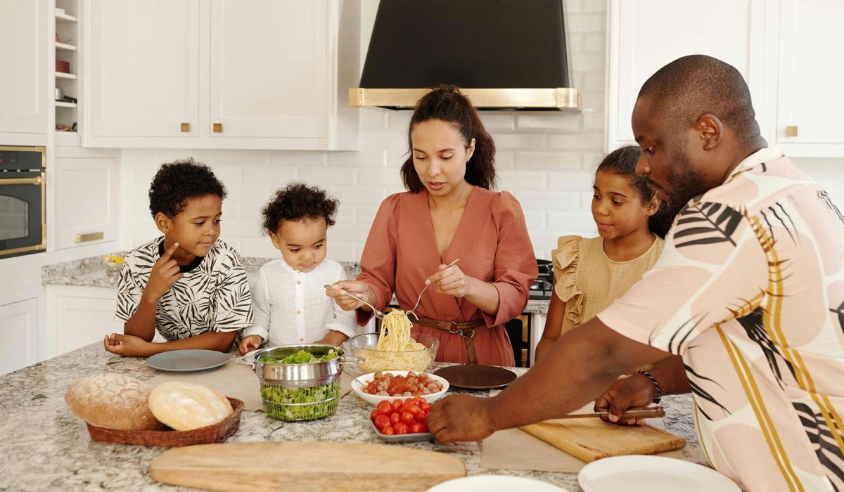 Family in kitchen with mother serving pasta