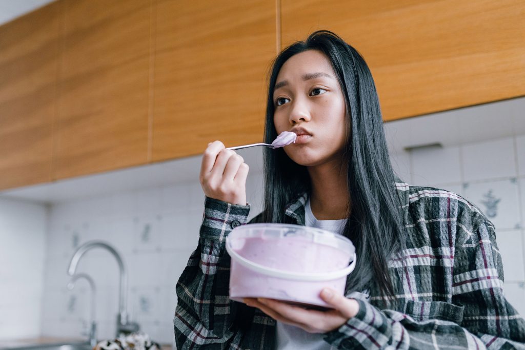 Woman standing in kitchen eating ice cream out of container