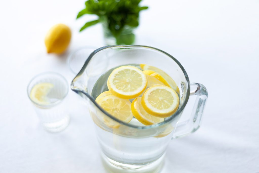 A pitcher of water with lemon slices and a glass next to it.